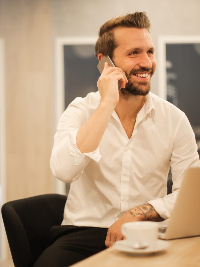 Smiling formal male with laptop chatting via phone